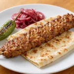 Adana Kebab – Pikantní mleté jehněčí nebo hovězí maso vytvarované na široké kovové jehle a grilované nad otevřeným ohněm.