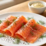 Gravlax – Skandinavischer Lachs, eingelegt in Salz, Zucker und Dill, in dünne Scheiben geschnitten und serviert mit Senfsauce und Brot.